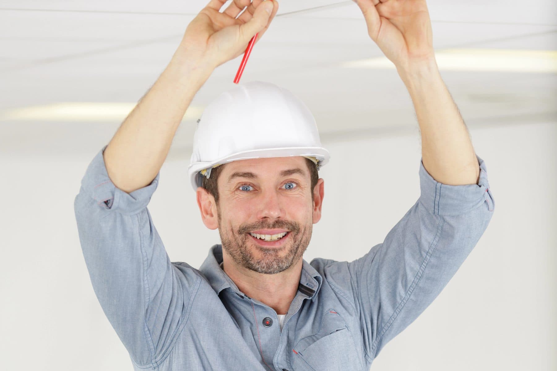 A technician on a ladder installing equipment in an office ceiling